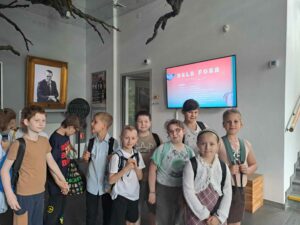 grupa dzieci stoi w holu Teatru Arlekin, w tle ekran z tytułem przedstawienia