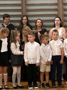 Na zdjęciu znajduje się grupa pięciorga dzieci w towarzystwie Pani Dyrektor, która pochyla się w ich stronę, rozmawia z nimi i podaje im rękę